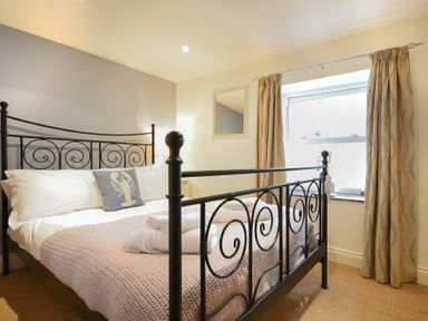 A bedroom with a metal framed bed a knitted blanket folded towels a pillow with a lobster design and a window with curtains at Mariners House in Alnmouth