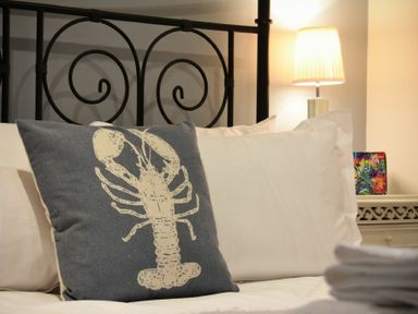 A bed with white pillows and a cushion with a lobster design and a lamp on a bedside table at Mariners House in Alnmouth