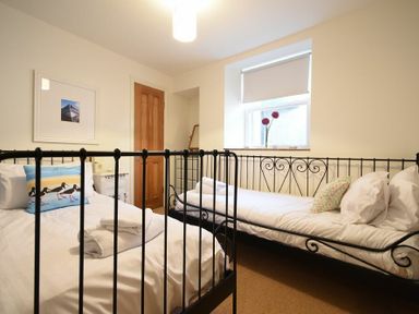A bedroom with two single beds a window with flowers on the sill and a wooden door at Mariners House in Alnmouth