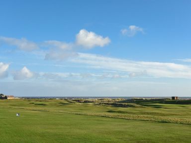 A golf course with green grass and distant buildings under a blue sky at Mariners House in Alnmouth