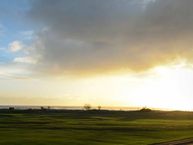 A grassy field with small trees and an ocean horizon under a cloudy sky at Mariners House in Alnmouth
