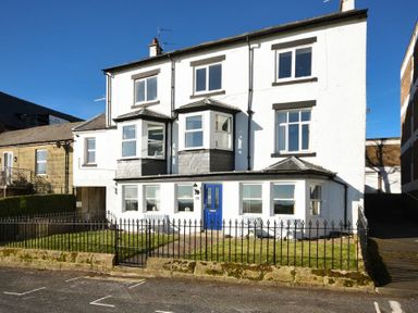 A white three-story house with a blue door and iron fence in front at Mariners House in Alnmouth
