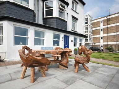 An outdoor patio area with wooden table and chairs outside a white building with blue door at Mariners House in Alnmouth