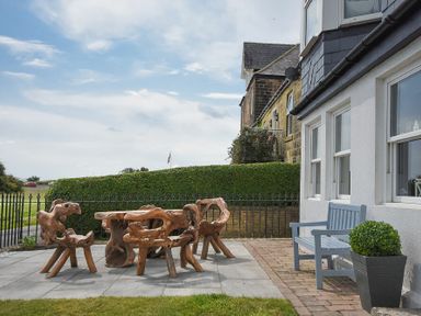 An outdoor patio with wooden furniture and a blue bench next to a white building at Mariners House in Alnmouth