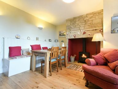 A dining area with a wooden table and chairs next to a fireplace and a pink sofa at Farne View Cottage in Seahouses