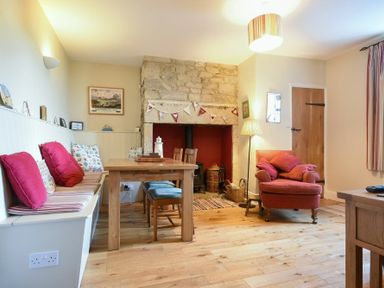 A dining area with wooden table and chairs next to a stone fireplace and an armchair at Farne View Cottage in Seahouses