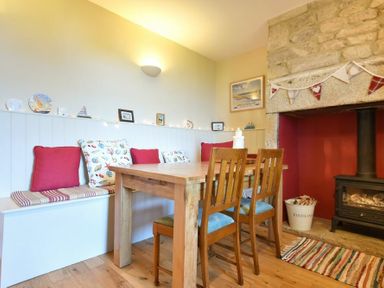 A dining area with a wooden table and chairs bench seating with cushions and a stone fireplace at Farne View Cottage in Seahouses