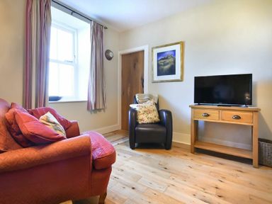 A sitting room with a red sofa a leather armchair a wooden TV stand with a television and a framed picture on the wall at Farne View Cottage in Seahouses