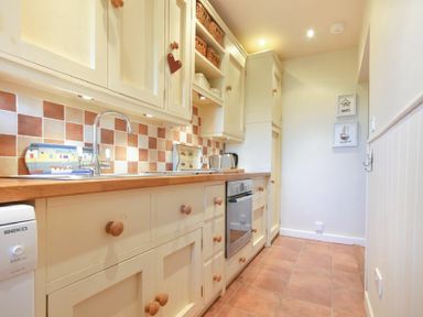 A galley kitchen with cream cabinets wooden knobs a tiled floor and wall tiles at Farne View Cottage in Seahouses
