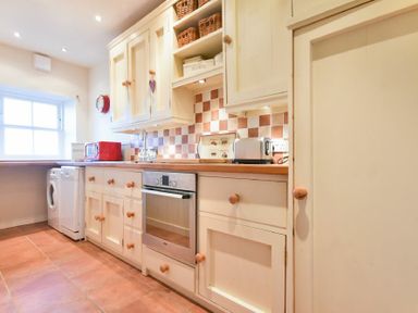 A kitchen with cream cabinets a countertop oven toaster microwave washing machine and window at Farne View Cottage in Seahouses