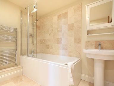 A bathroom with a bathtub shower combination a white sink and a towel rack at Farne View Cottage in Seahouses