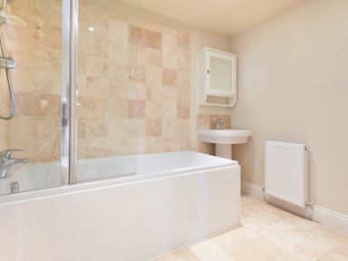 A bathroom with a bathtub shower combo sink with cabinet and radiator at Farne View Cottage in Seahouses