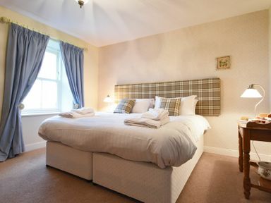A bedroom with a double bed and plaid headboard blue curtains and a wooden table with a lamp at Farne View Cottage in Seahouses