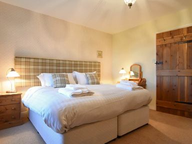 A bedroom with a double bed with plaid headboard two bedside tables lamps a wooden door and a dressing table at Farne View Cottage in Seahouses