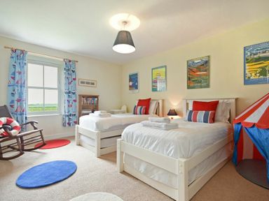 A bedroom with two white beds blue and red pillows a wooden rocking chair and a small tent at Farne View Cottage in Seahouses