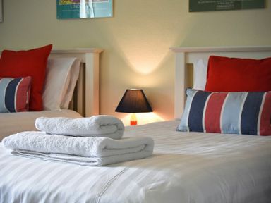 A bedroom with two beds dressed in white linens and red and striped pillows with folded white towels on one bed at Farne View Cottage in Seahouses