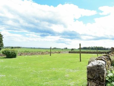 A grassy garden with stone walls and wooden posts at Farne View Cottage in Seahouses