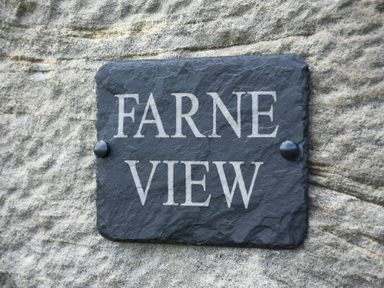A slate stone plaque with the text Farne View mounted on a textured stone wall at Farne View Cottage in Seahouses