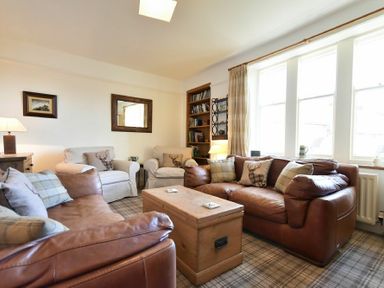 A living room with brown leather sofas beige armchairs wooden chest and bookshelf at Whistlewood in Bamburgh