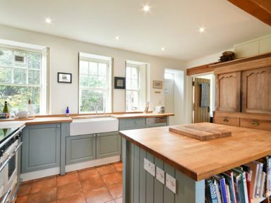 A kitchen with blue cabinets wooden countertops a large wooden island and three windows at Whistlewood in Bamburgh
