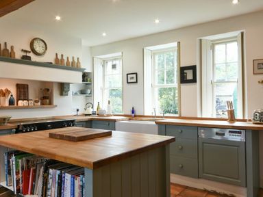 A kitchen with wooden countertops a kitchen island cookbooks and three windows at Whistlewood in Bamburgh