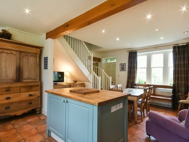 A living room with dining table wooden cupboard kitchen island and staircase at Whistlewood in Bamburgh