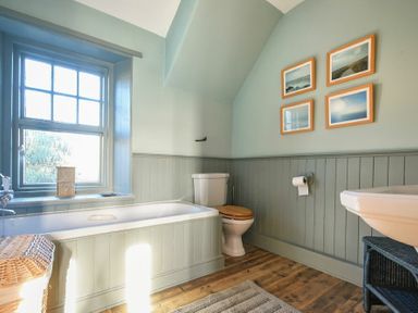 A bathroom with a bathtub a toilet a sink framed pictures on the wall and a wicker basket at Whistlewood in Bamburgh