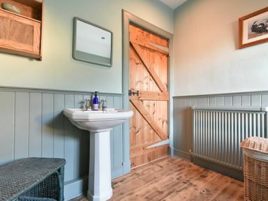 A bathroom with a pedestal sink mirror wooden door radiator and wicker basket at Whistlewood Bamburgh