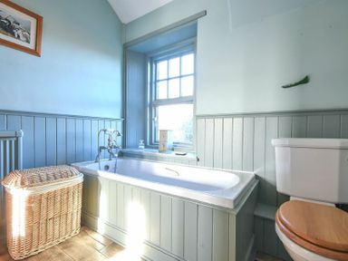 A bathroom with a bathtub a wicker laundry basket a toilet and a window at Whistlewood in Bamburgh