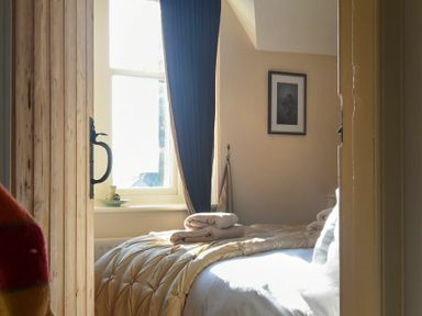 A bedroom with a bed covered with a comforter and folded towels by a window with curtains at Whistlewood in Bamburgh