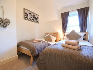 A bedroom with two single beds beside a window with brown curtains at Whistlewood in Bamburgh