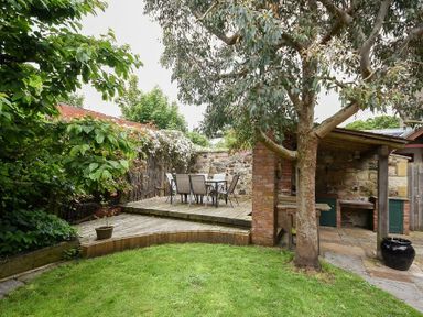 A garden with a wooden deck dining area and a covered stone barbecue at Whistlewood in Bamburgh