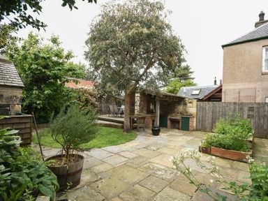 A backyard with a stone patio a tree a raised garden bed and outdoor seating area at Whistlewood in Bamburgh