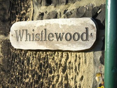 A wooden sign with Whistlewood engraved on a stone wall at Whistlewood in Bamburgh