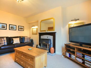 A living room with a black sofa cushions wooden coffee table fireplace and a television on a wooden stand at Castle View Warkworth
