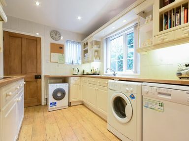A kitchen with white cabinets wooden countertops a washing machine dishwasher and window at Castle View Warkworth