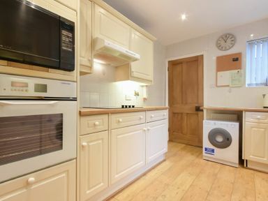 A kitchen with cream cabinets wooden countertops oven microwave washing machine and a wooden door at Castle View Warkworth