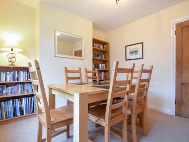 A dining room with a wooden table and six chairs, bookcases, a lamp, a wall mirror, and a framed picture at Castle View in Warkworth