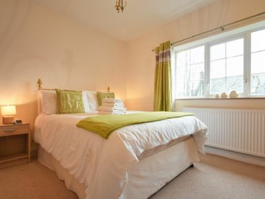 A bedroom with a bed with green cushions and blanket beside a window with green curtains at Castle View Warkworth