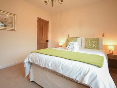 A bedroom with a bed, green cushions, folded towels, bedside tables with lamps and a wooden door at Castle View Warkworth