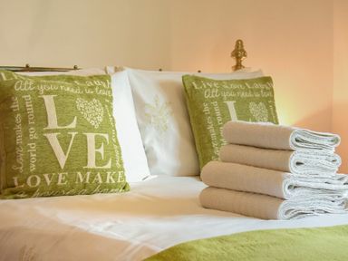 A bed with green love themed cushions and a stack of folded white towels at Castle View Warkworth