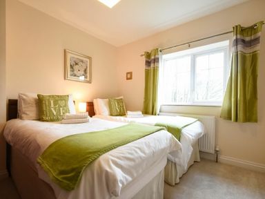 A bedroom with two single beds with green throws and pillows and a window with green curtains at Castle View Warkworth