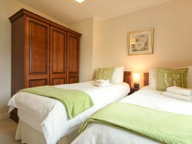 A bedroom with two single beds with green throws and pillows a wooden wardrobe and a bedside table with a lamp at Castle View Warkworth