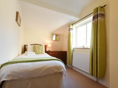 A bedroom with a single bed green curtains and a wooden dresser at Castle View Warkworth