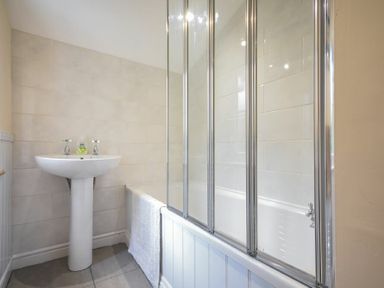 A bathroom with a pedestal sink and a bathtub with a glass shower screen at Castle View Warkworth