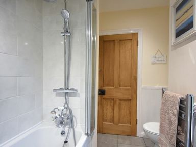 A bathroom with a shower over a bathtub a wooden door a toilet a towel on a rail and a painting on the wall at Castle View Warkworth