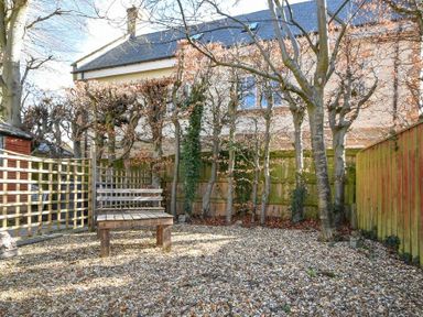A gravel garden with a wooden bench and small trees along a wooden fence at Castle View Warkworth