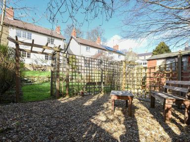 A garden area with wooden trellis, bench, and table in front of houses at Castle View Warkworth