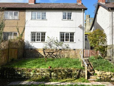 A backyard garden with a stone retaining wall wooden table and chairs and stairs leading to a gate at Castle View Warkworth