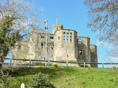 An old stone castle with multiple windows on a grassy hill surrounded by trees at Castle View Warkworth